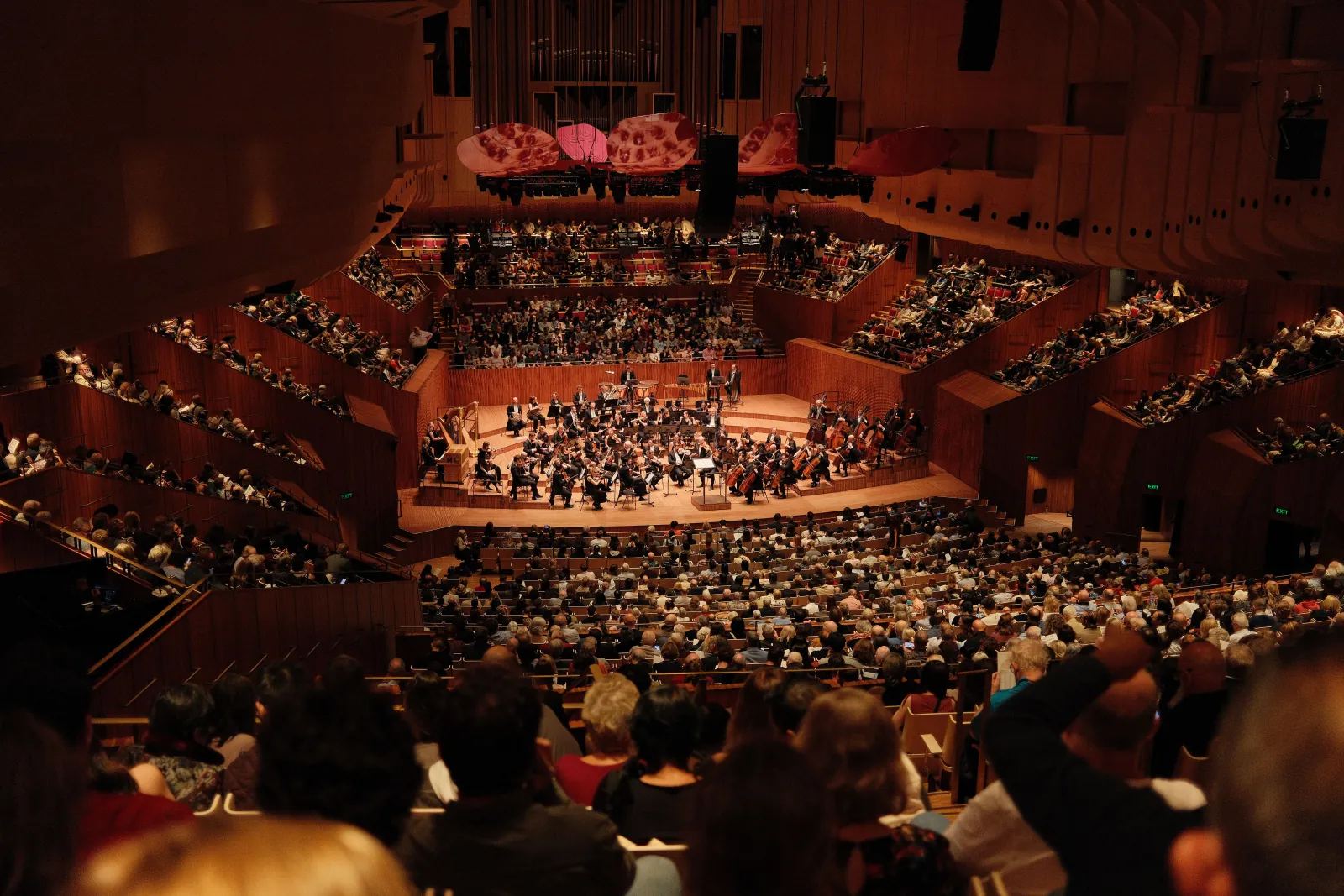 Full audience seated around the stage of a concert hall during an orchestral performance