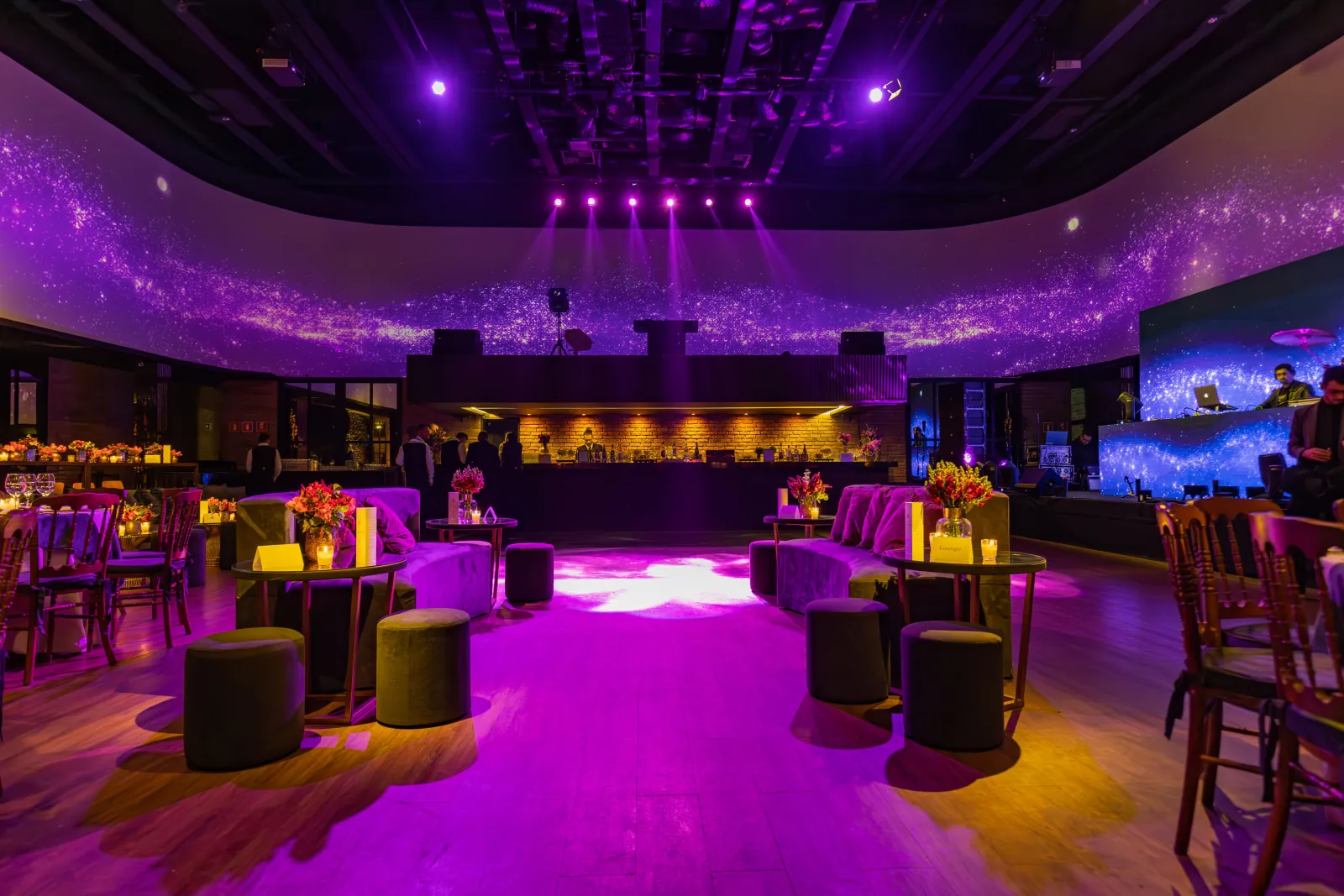 Purple-lit event space with lounge seating and a bar before guests arrive