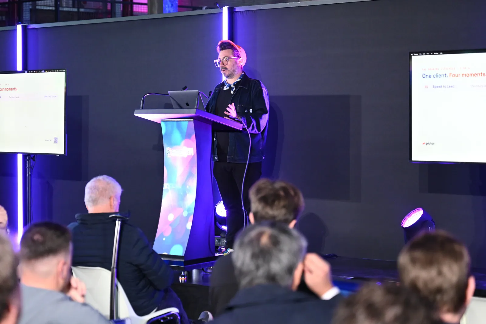 PBX Europe 2026 Recap: Both Talks, Both Decks 2 Nicholas Rhodes at the podium delivering the PBX Europe 2026 keynote on AI tools for photo booth businesses, audience in the foreground